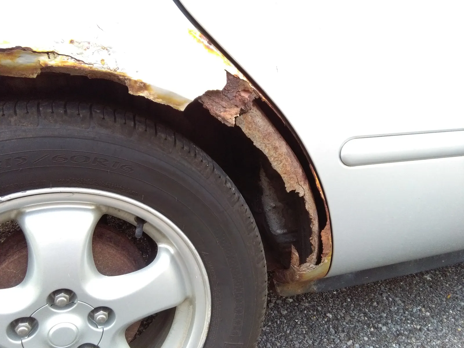 Passage de roue d'une voiture rongé par la rouille jusqu'à la tôle nue.