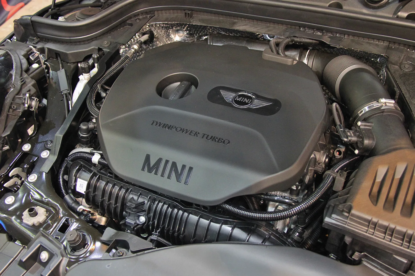 Compartiment moteur ouvert d'une Mini, cache-moteur floqué du logo Mini et de la mention TwinPower Turbo.
