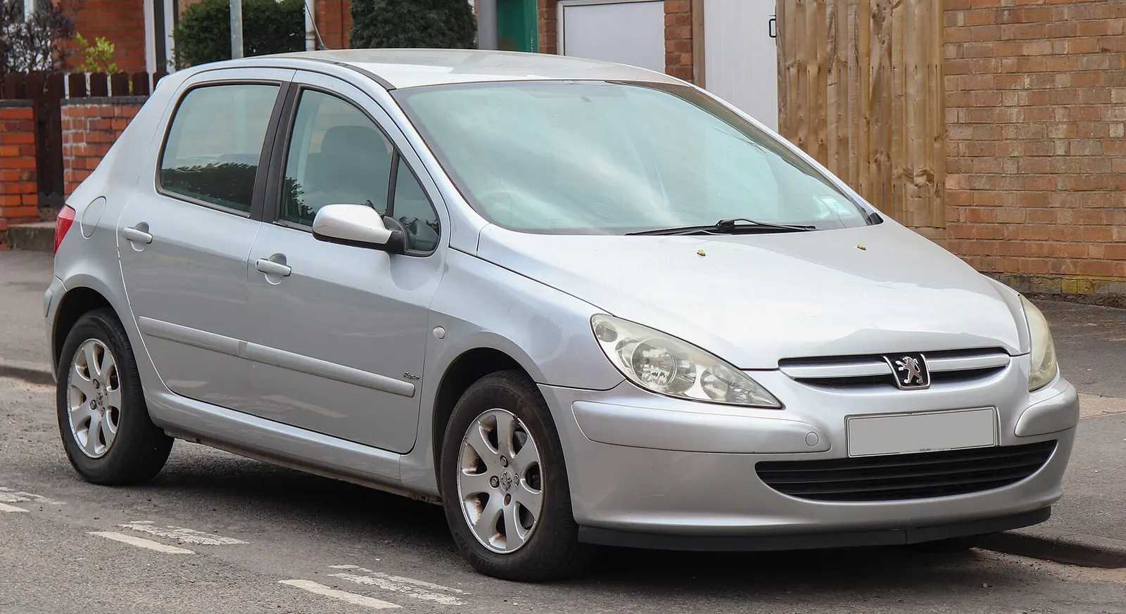 Peugeot 307 cinq portes gris argent de 2002, vue de trois-quarts avant, garée dans une rue résidentielle.