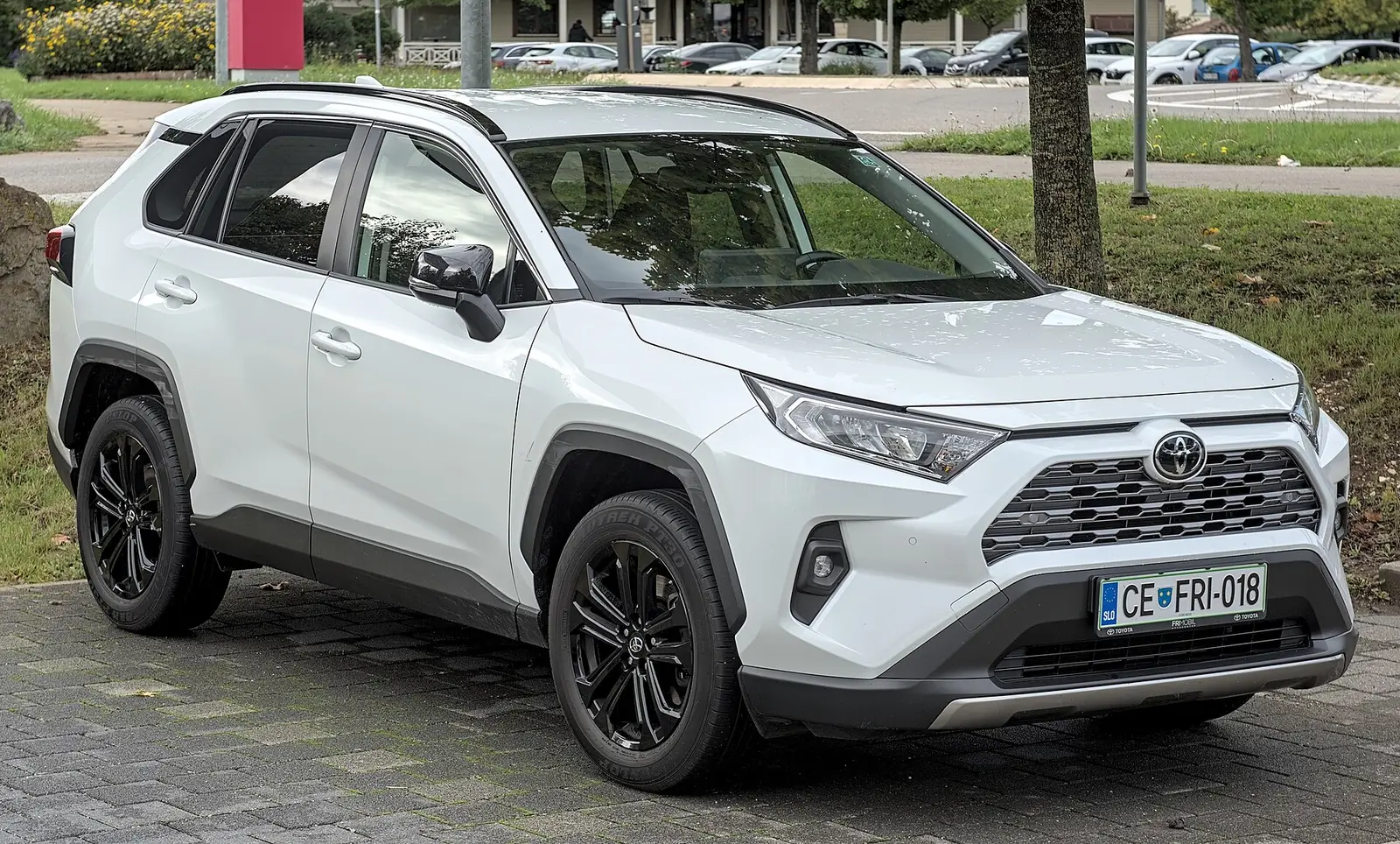 Toyota RAV4 hybride de cinquième génération blanc, jantes noires, vu de trois-quarts avant, garé sur un parking pavé.